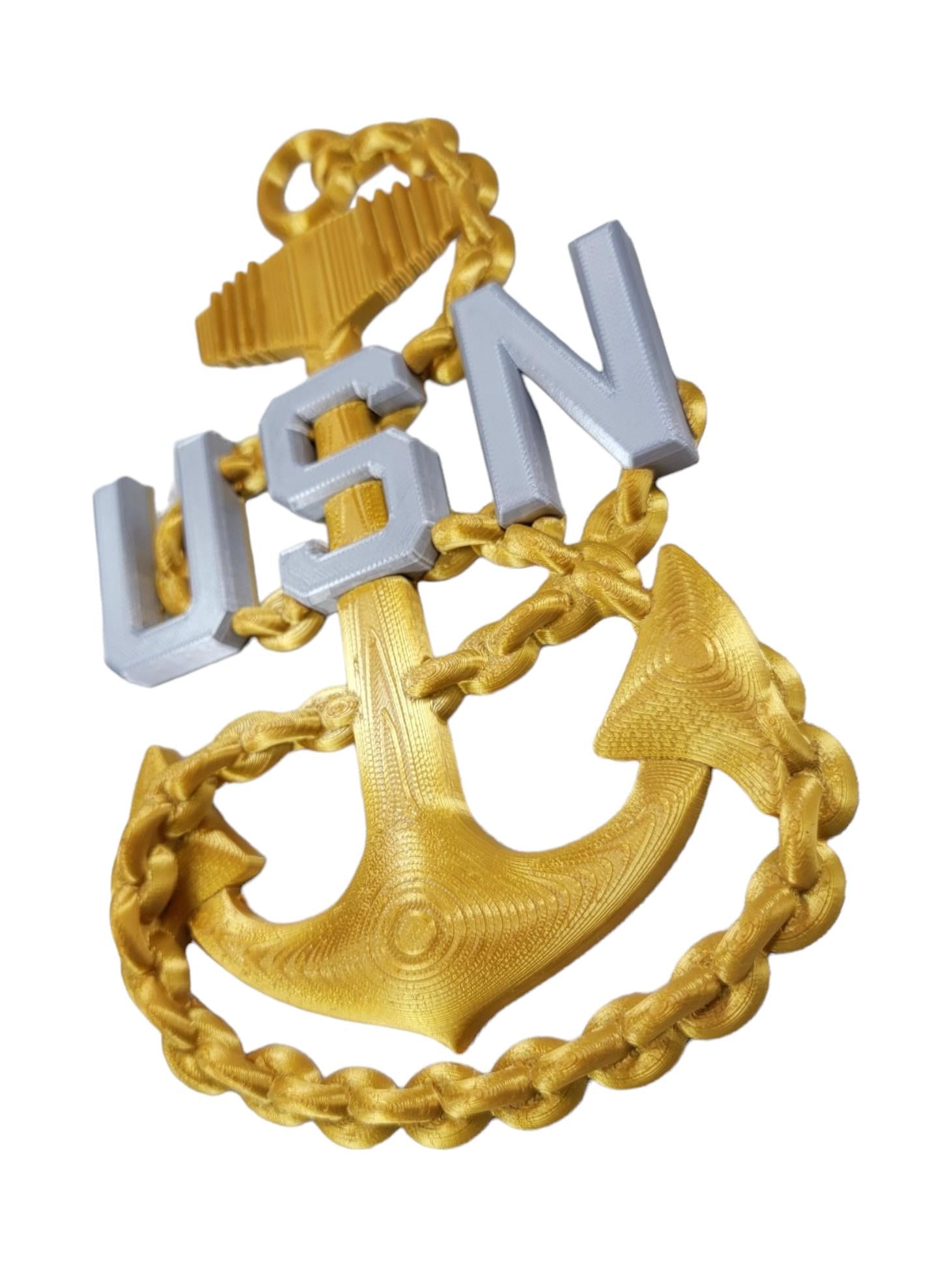 "US Navy E7 Chief rank insignia featuring a gold anchor with silver 'USN' letters, shown on a white background at a slight side angle."