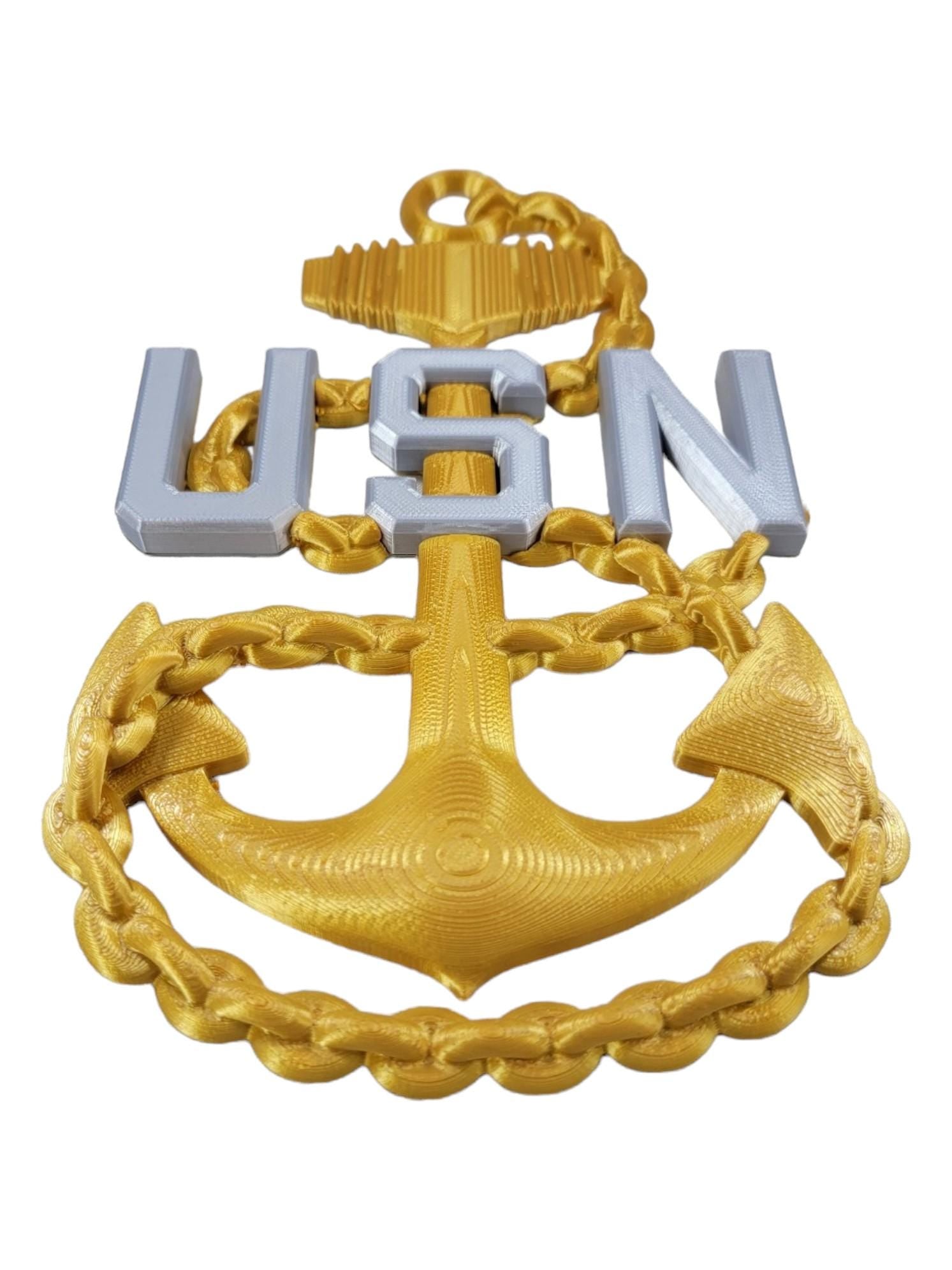 US Navy E7 Chief rank insignia with a gold anchor and silver 'USN' letters, displayed on a white background from a bottom-up angle.